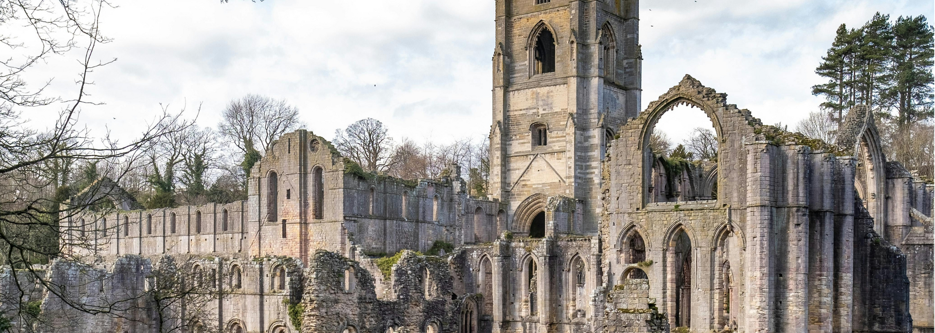 Ruined abbey with tall tower and arched openings under a cloudy sky.