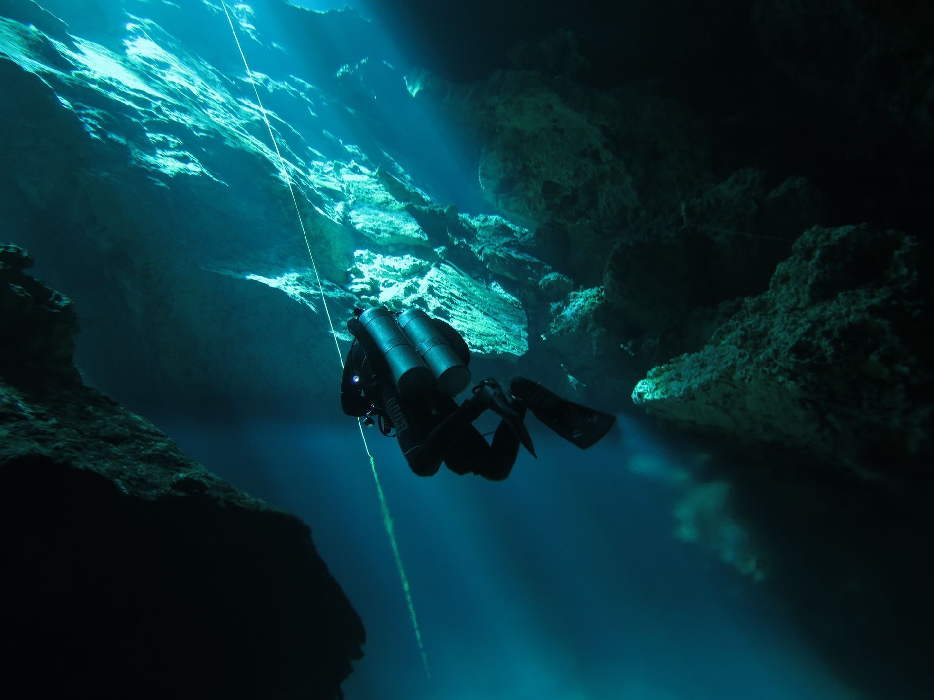 Scuba diver exploring an underwater cavern, illuminated by sunlight.