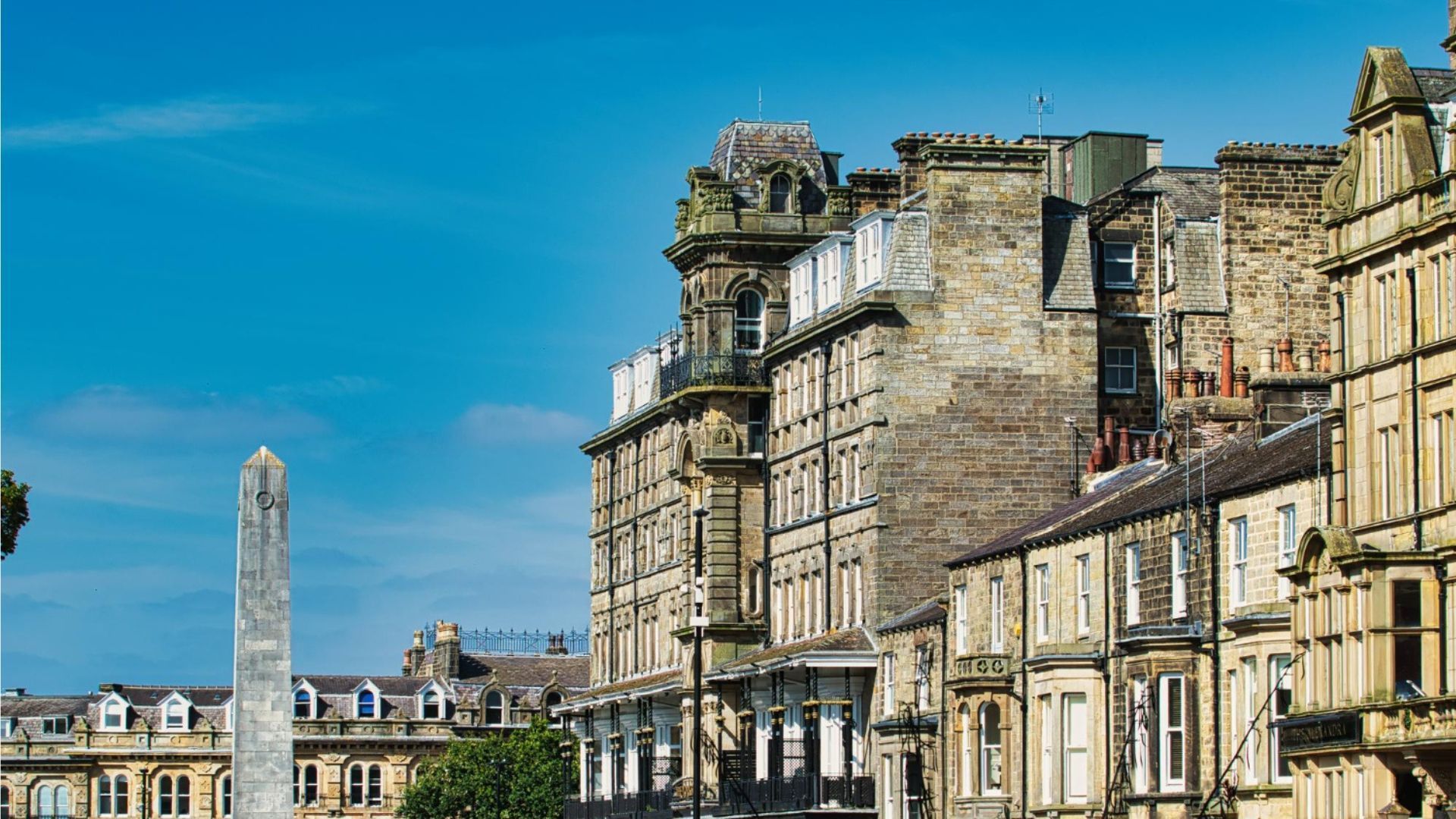 Stone buildings in a row under a blue sky, with an obelisk to the left.
