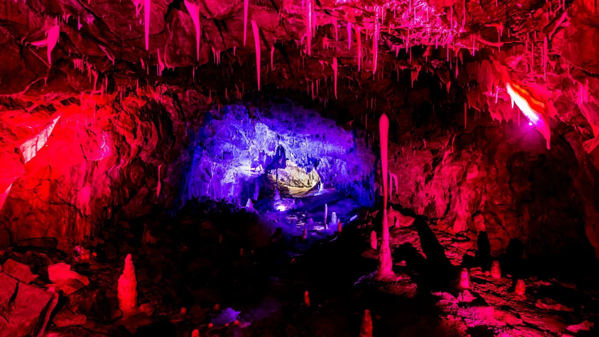 Cave interior lit with red and purple lights, stalactites and stalagmites visible.