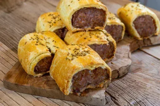 Sausage rolls on a wooden board, golden pastry, savory filling, herbs sprinkled on top.