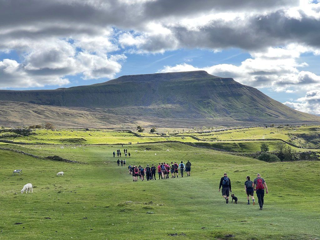 Hikers walking towards a large, green mountain under a cloudy sky.