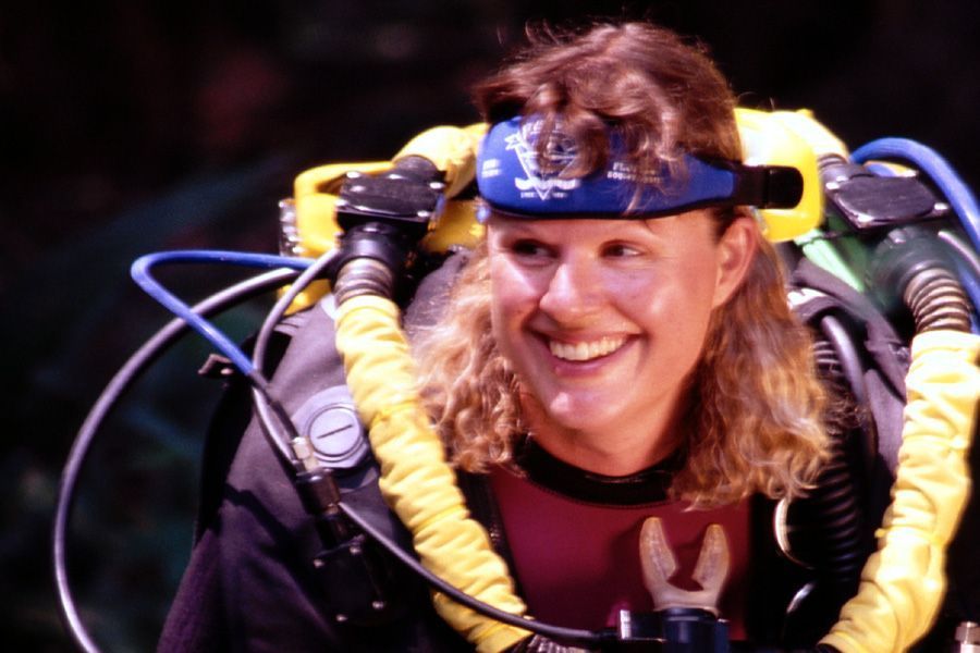 Scuba diver with blonde hair, wearing a diving apparatus and smiling.