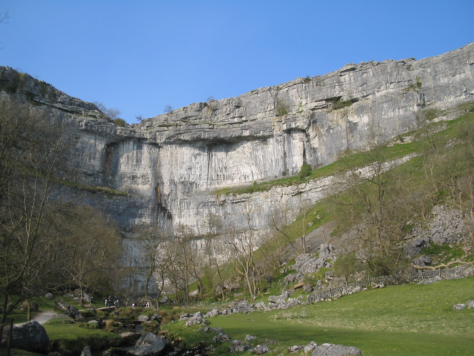 Limestone cliff face, grassy valley, blue sky, trees.