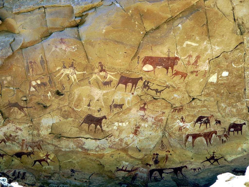 Cave painting depicting cattle, humans, and other animals in shades of red, brown, and white on a rock surface.