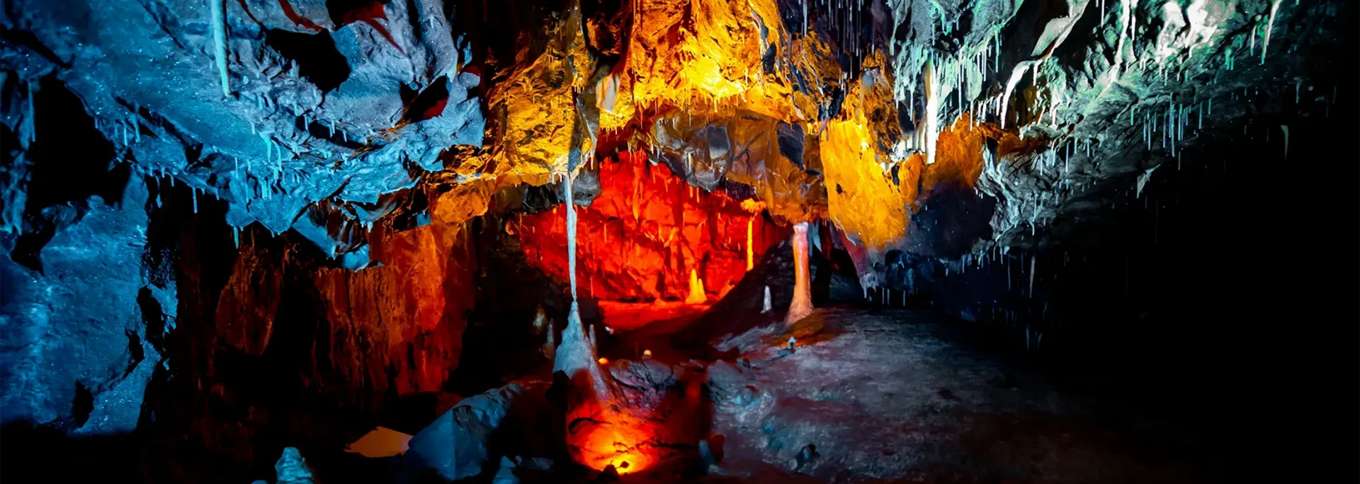 Cave interior with colorful lighting illuminating rock formations and stalactites.