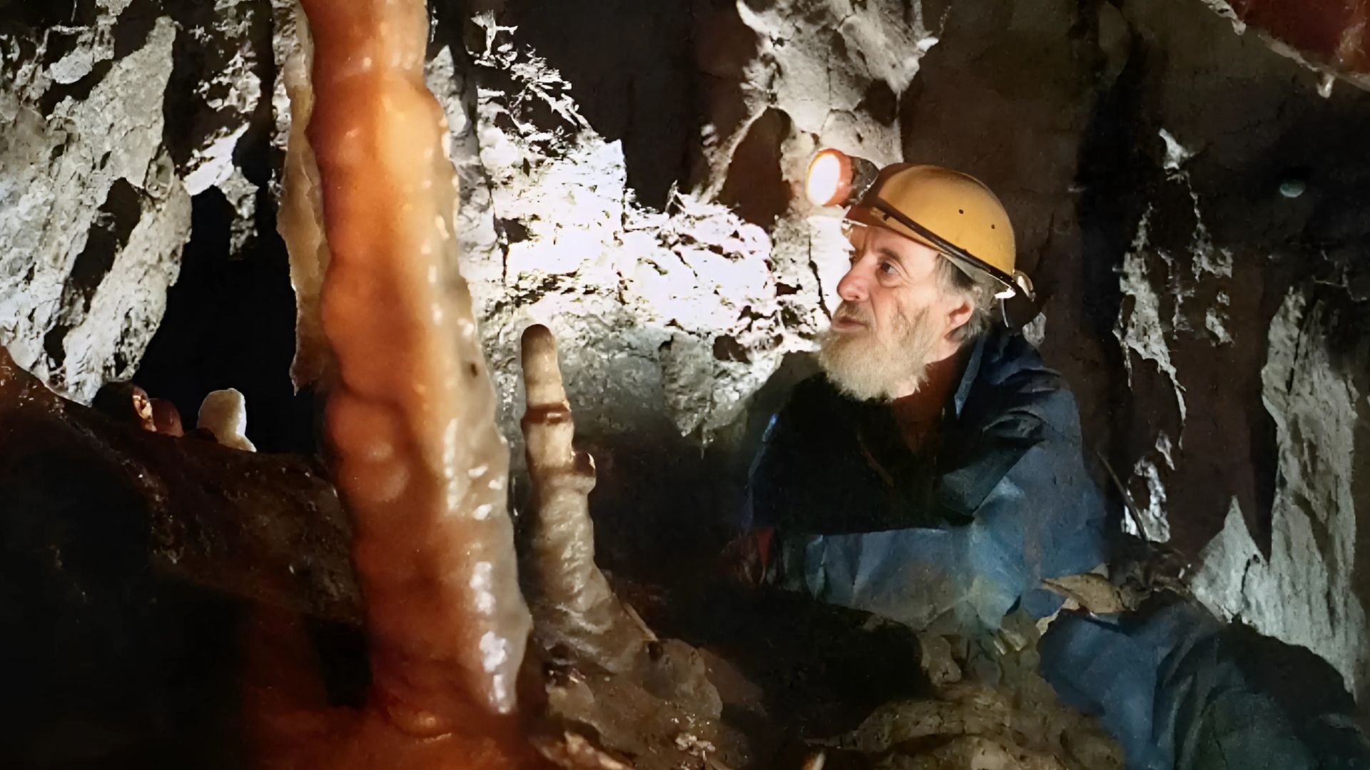 Man in hard hat examines cave formation with flashlight.