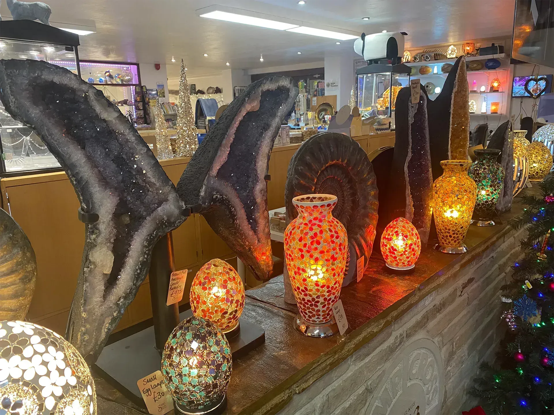Display of lit gemstone lamps and crystals in a shop, with a Christmas tree visible on the right.