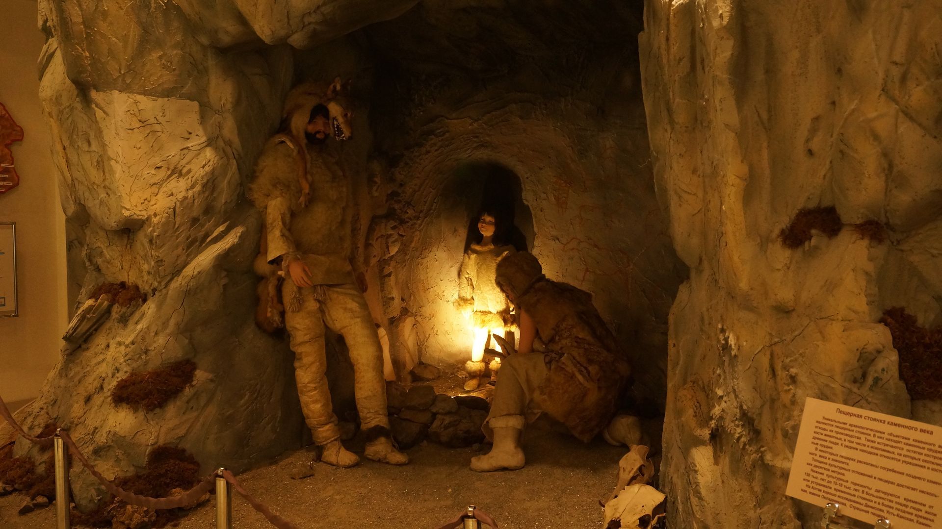 Cave diorama with figures illuminated by a torch. Two stand, one kneels, inside a rock formation.