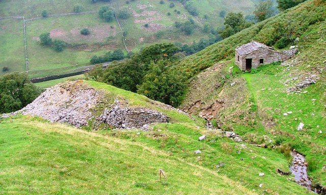 Stone building on a grassy hillside, overlooking a valley with a stream.