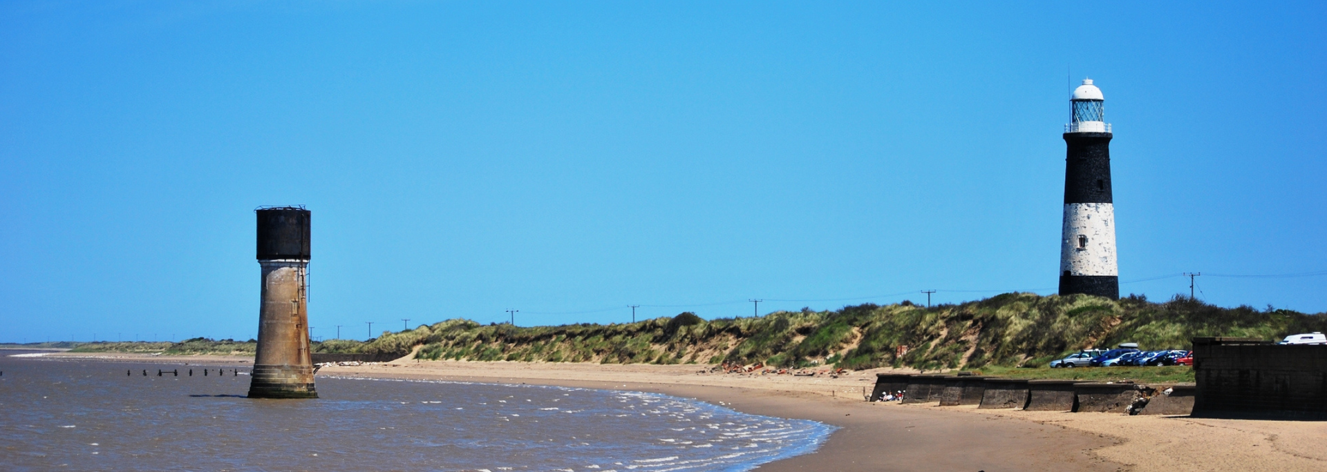 A lighthouse on a sandy beach under a clear blue sky.