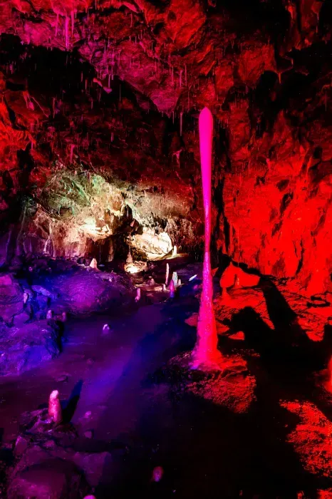 Red-lit cave with a bright pink stalactite-like formation and purple light reflecting on the floor