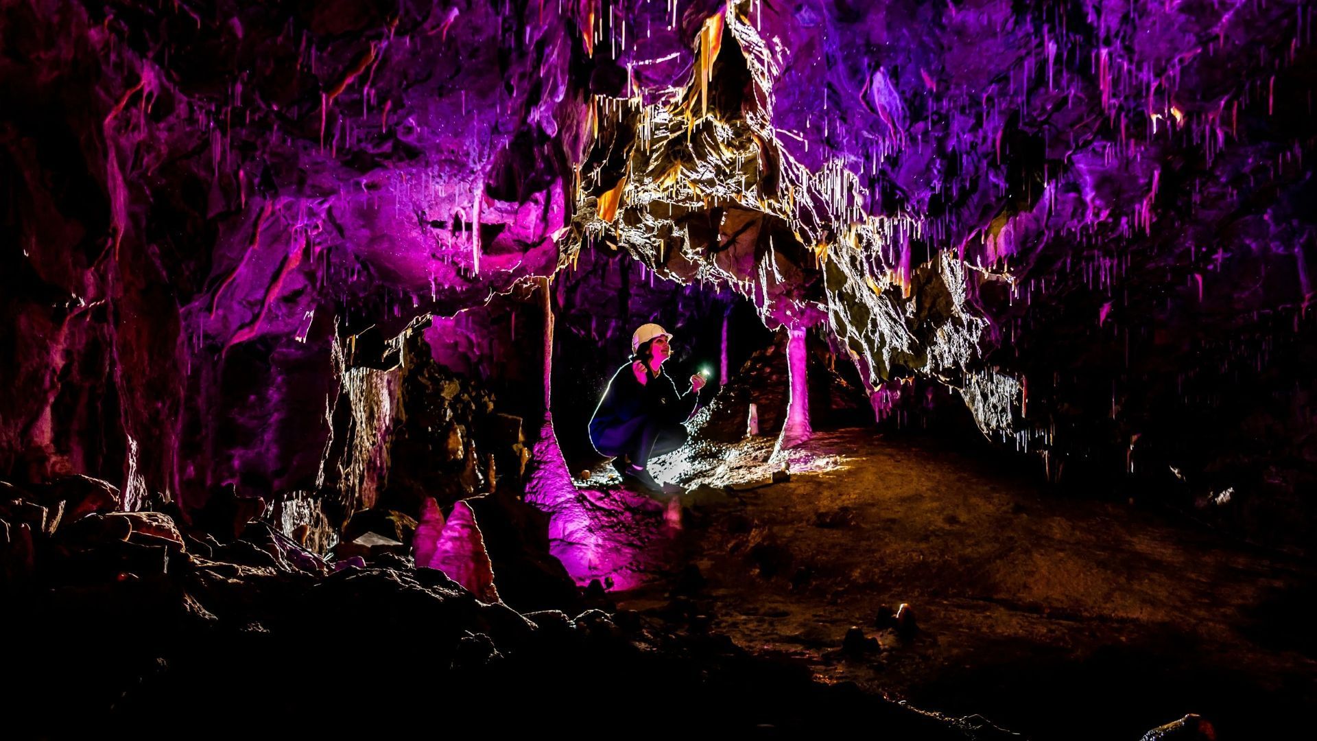 Person in cave lit with purple light, examining rock formations.