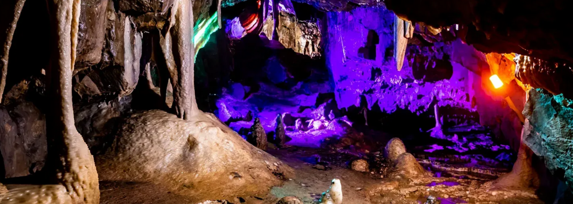 Cave interior illuminated with purple and orange lights, highlighting rock formations and water.