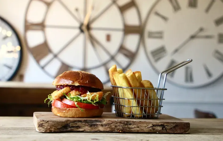 Burger with fries on a wooden board, in front of a clock.