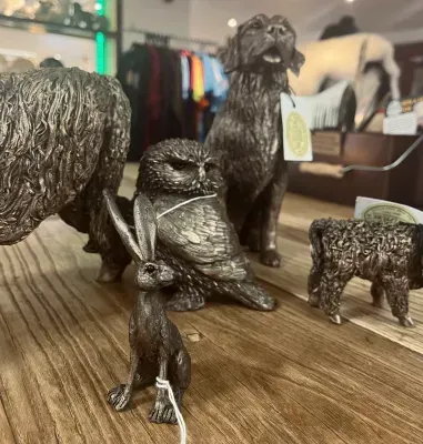 Bronze animal sculptures on a wooden surface: bear, owl, hare, dog, and calf.