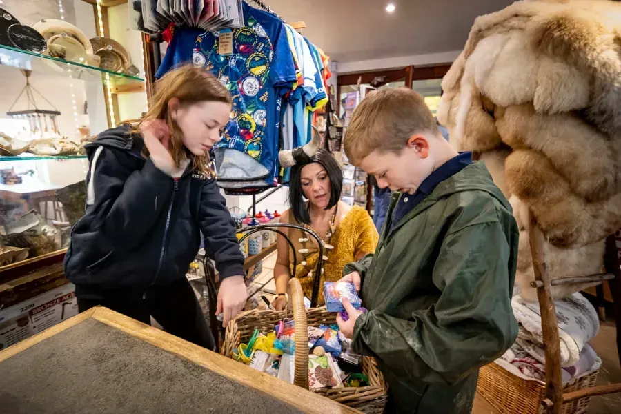 Two children and an adult looking at items in a wicker basket inside a shop.