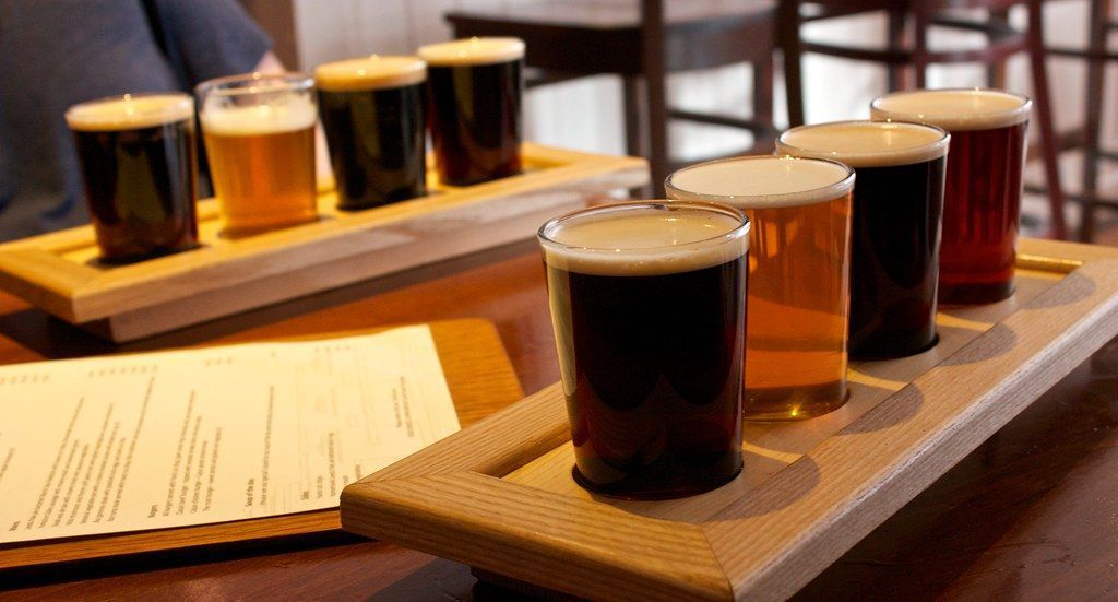 Two beer flights on wooden trays with six different beers in glasses.