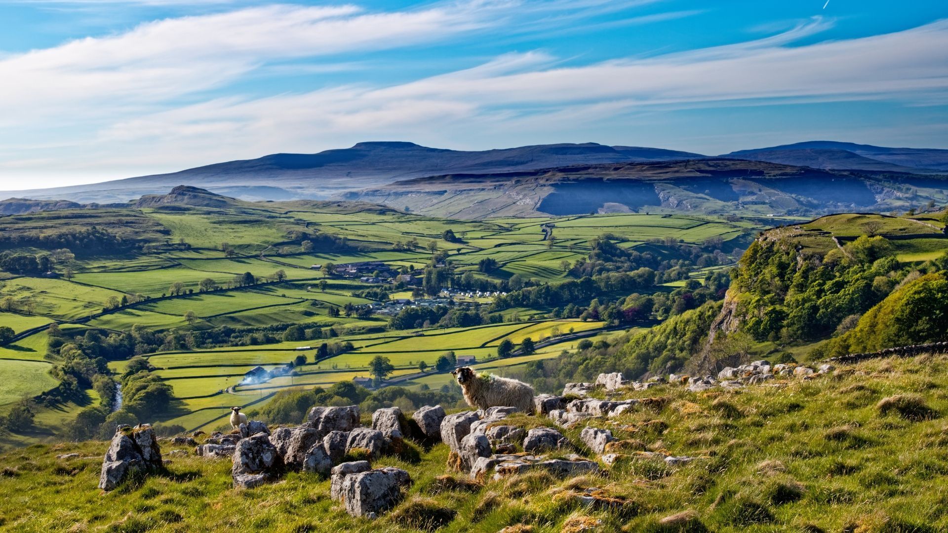 Rolling green hills, distant mountains, and blue sky. Rocky foreground.