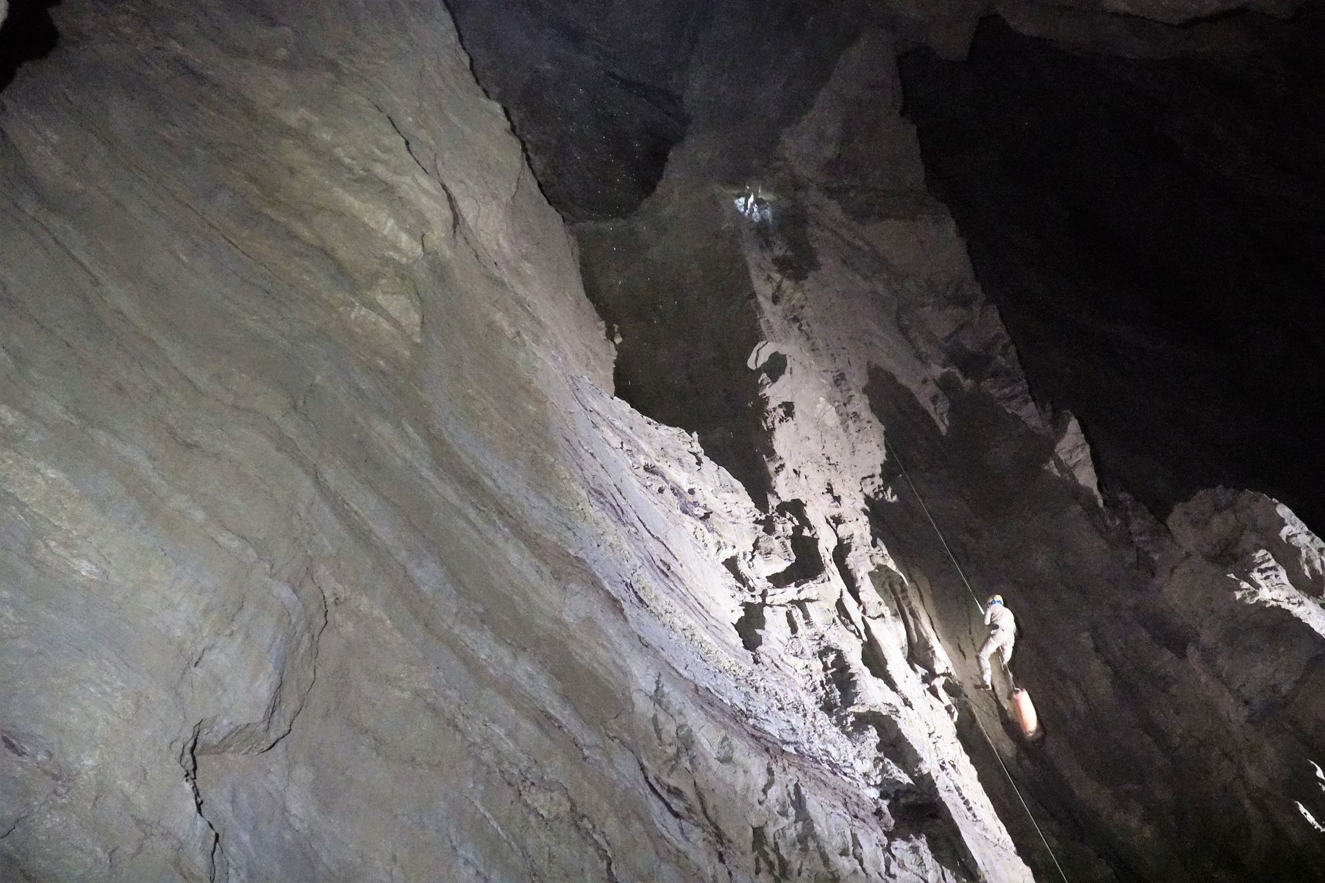 Dark cave interior with layered rock formations, angled upward toward a dimly lit opening.