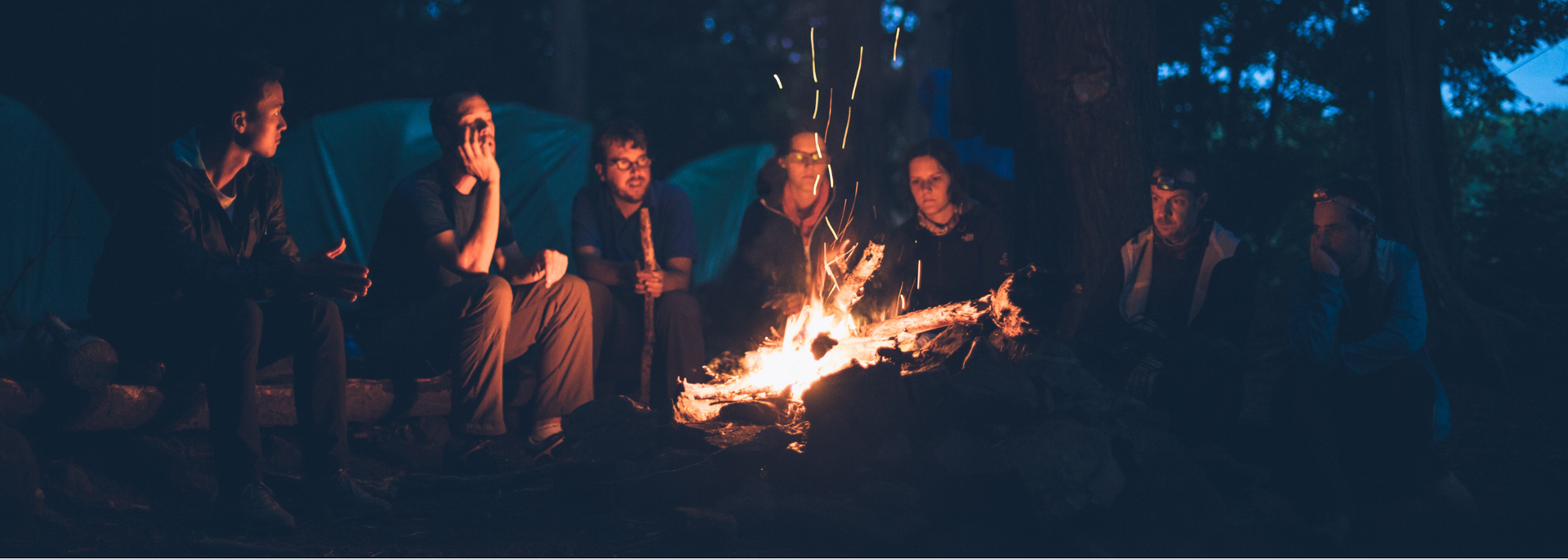Group of people gathered around a campfire in the forest at night.