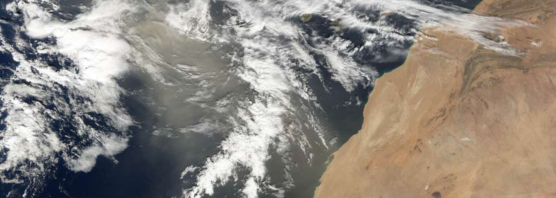 Satellite view of the coast of Africa, with ocean and clouds; shades of blue, brown, and white.