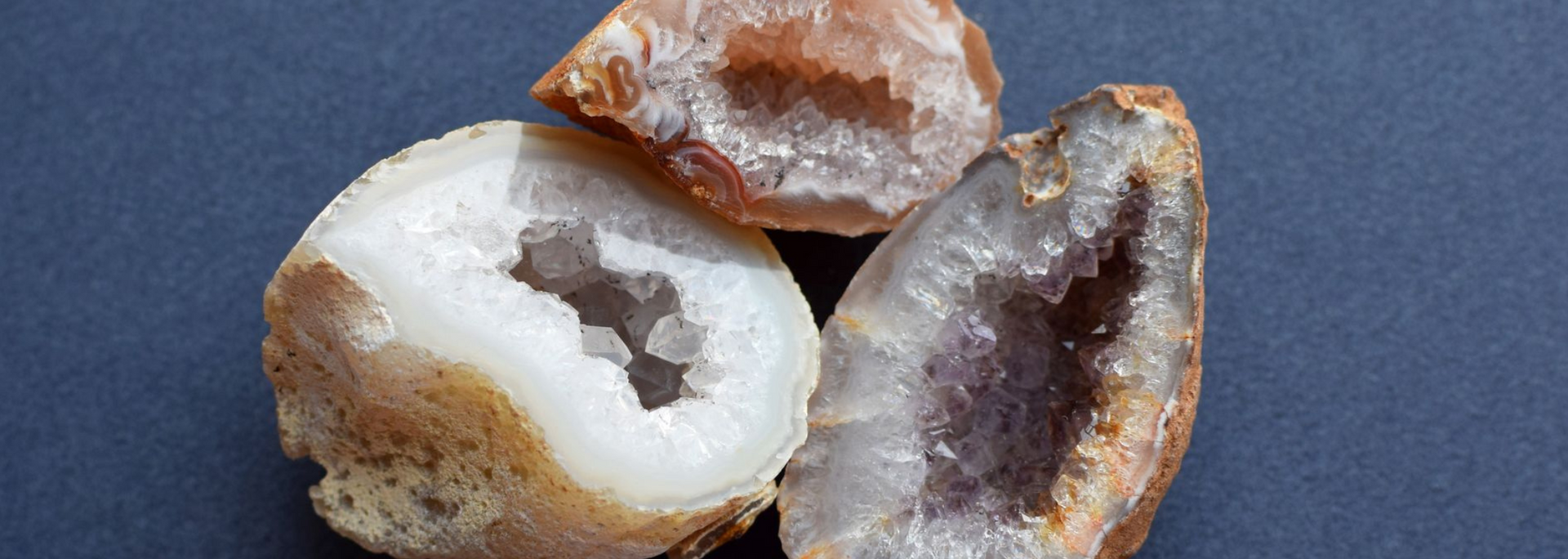 Three geodes against a dark blue background. The geodes are tan, white, and purple with crystal formations inside.
