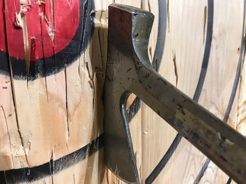 Axe embedded in a wooden target, red and black circles visible.