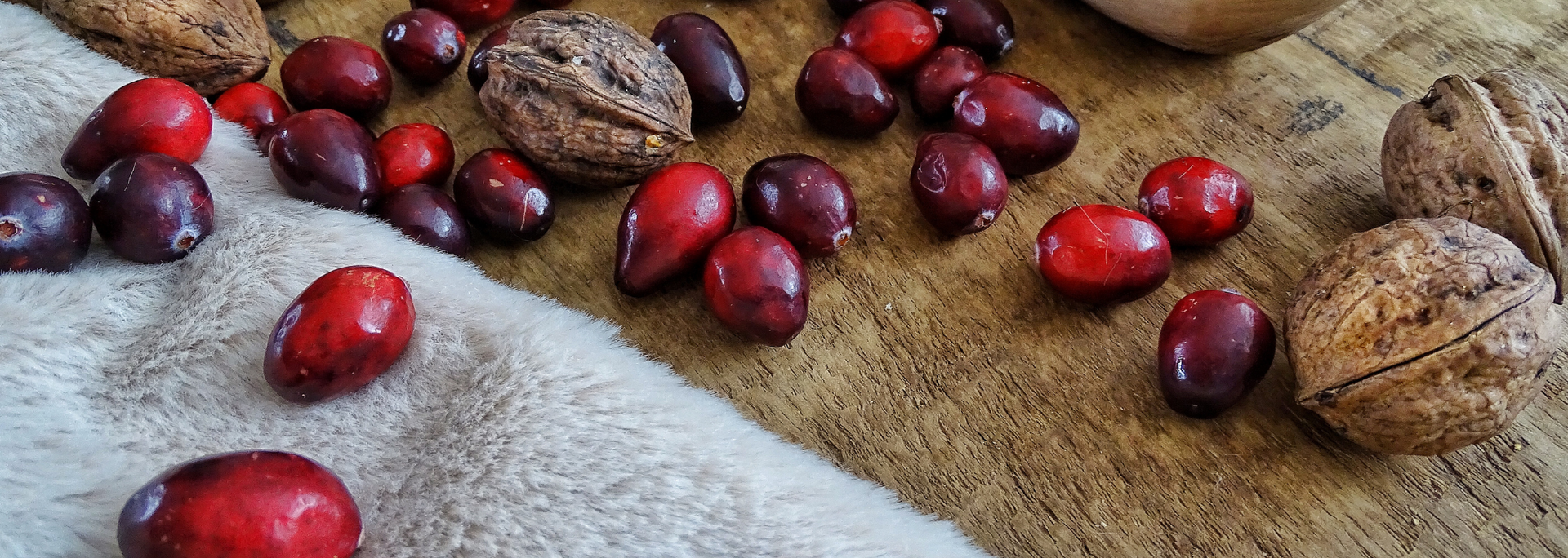 Cranberries and walnuts on a wooden surface and a soft, white cloth.