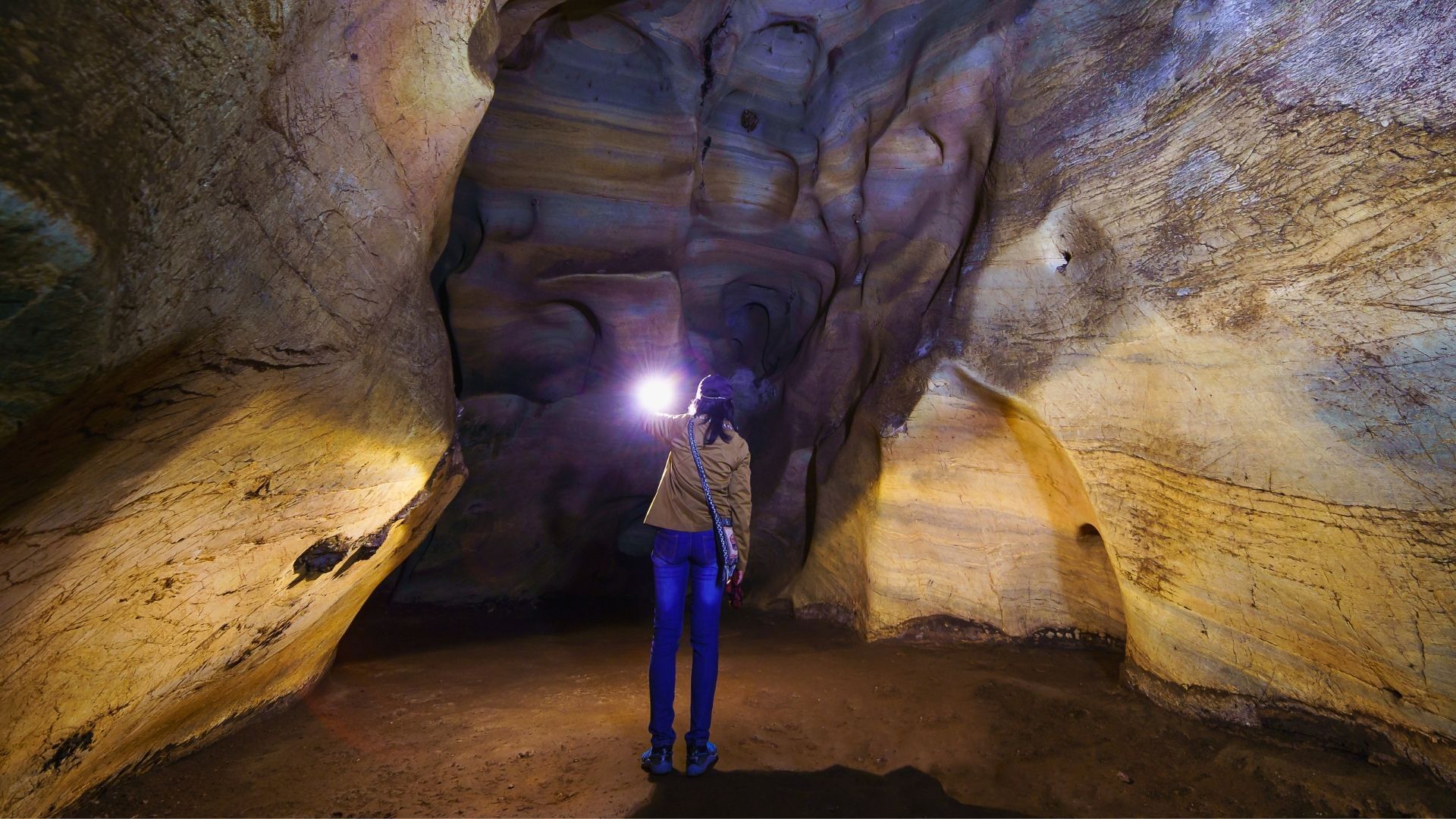 Person with a headlamp in a sandstone cave, looking upwards; warm lighting.