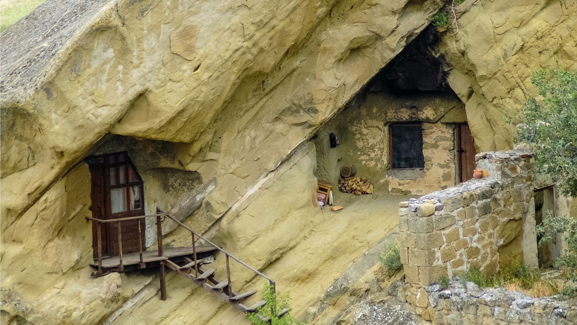 Cave dwellings carved into a light-colored rock face with wooden balconies and stone structures.