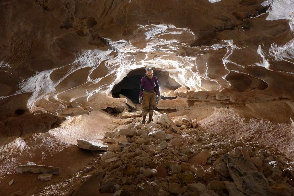 Person in a cave, illuminated by light. Brown and white rock formations surround them.