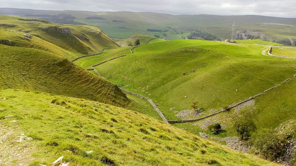 Green rolling hills with a stone wall and valley in a natural landscape.