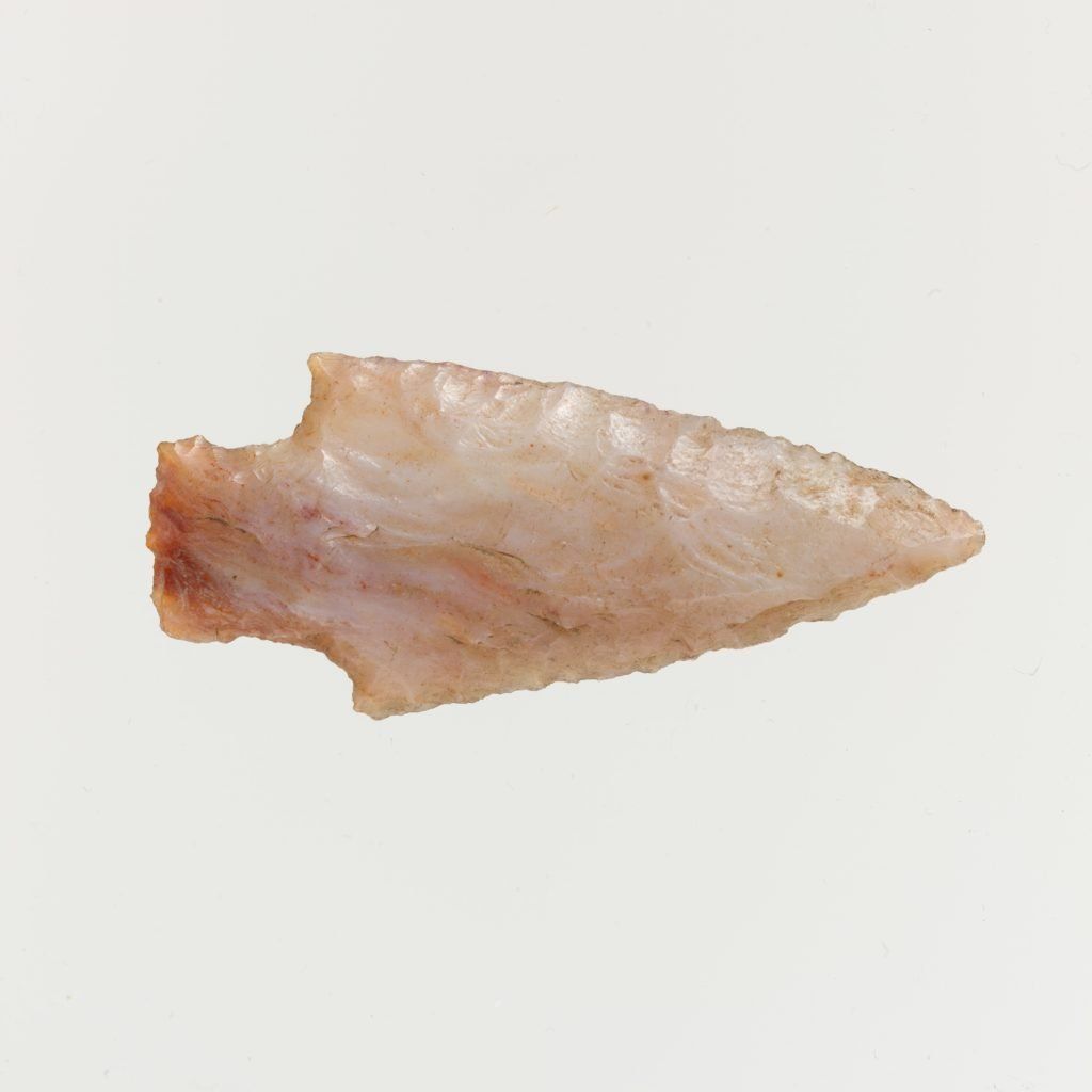Arrowhead made of light-colored stone, with a broken base and sharp tip.