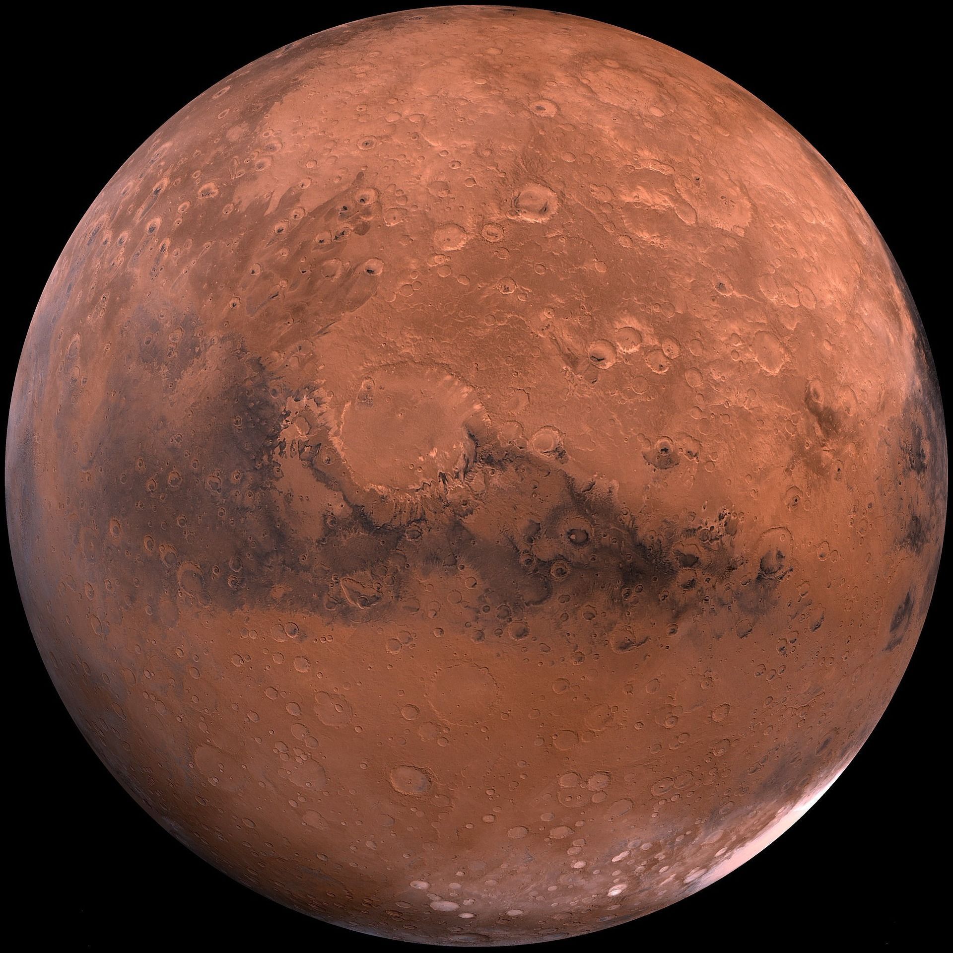 Reddish-brown Mars with dark, cratered regions and polar ice cap, illuminated by sunlight.