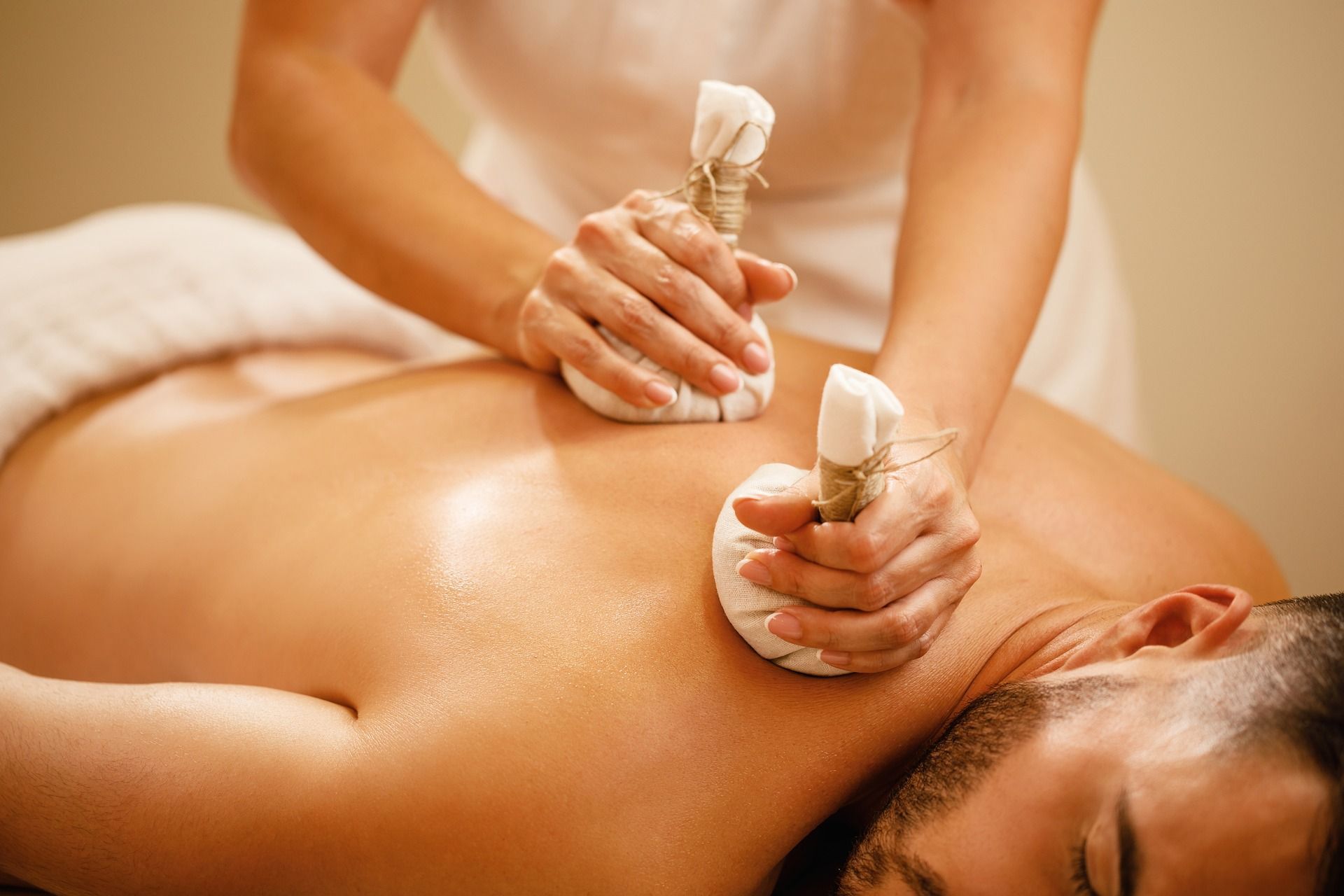 Person receiving herbal compress massage on their back in a spa setting.