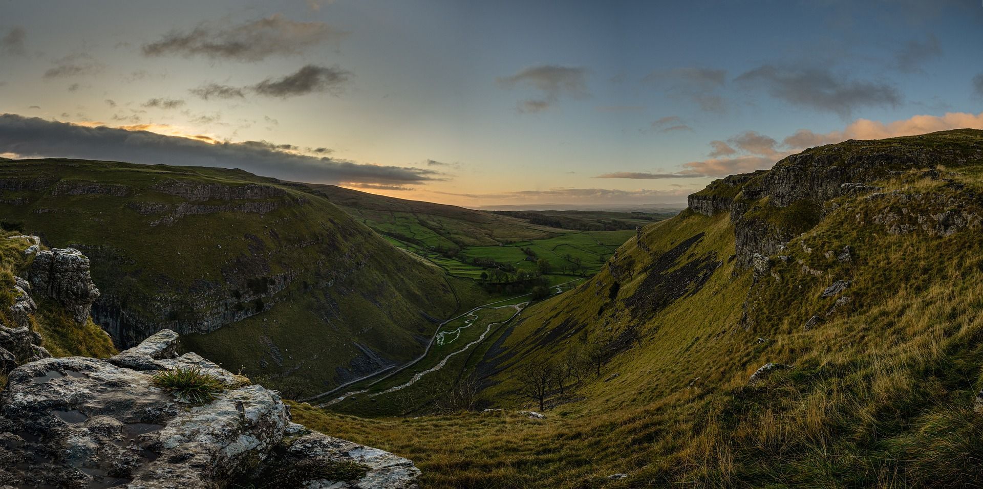 Panoramic view of a green valley between rocky hills under a cloudy sky at dusk.