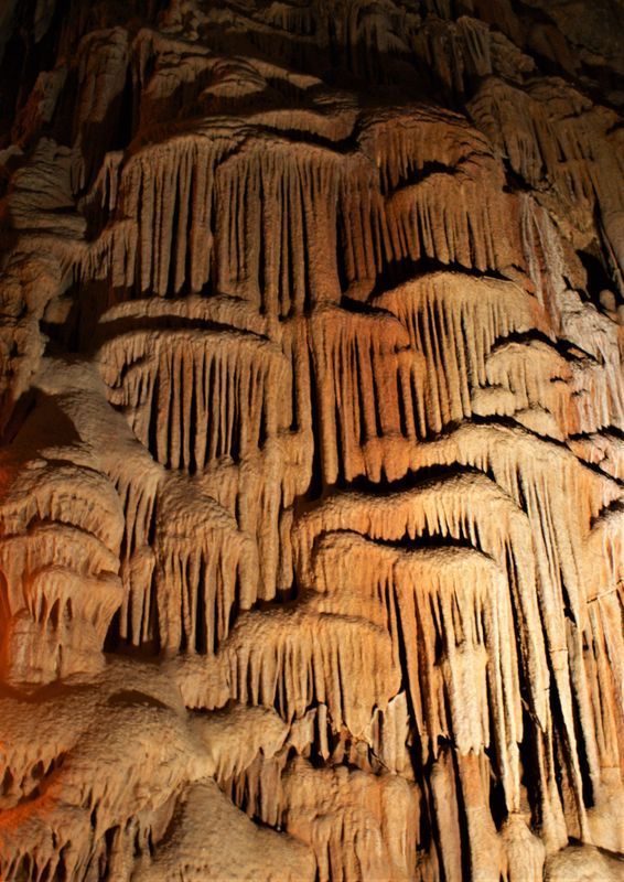 Lit cave wall with orange-brown stalactites and flowstone formations