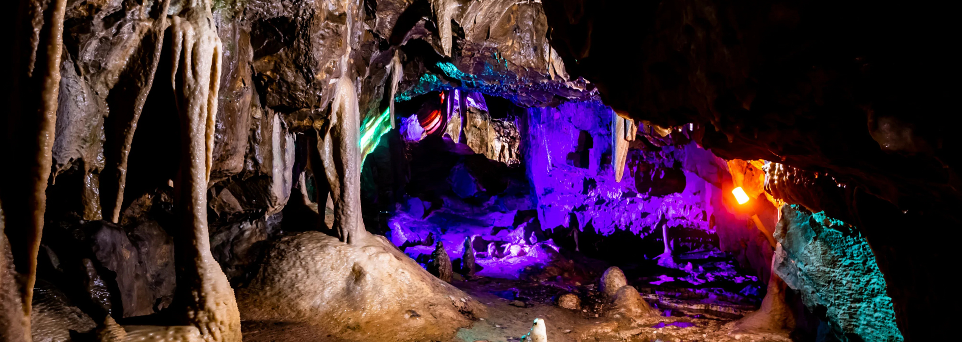 Inside a cave, colorful lights illuminate stalactites and formations.
