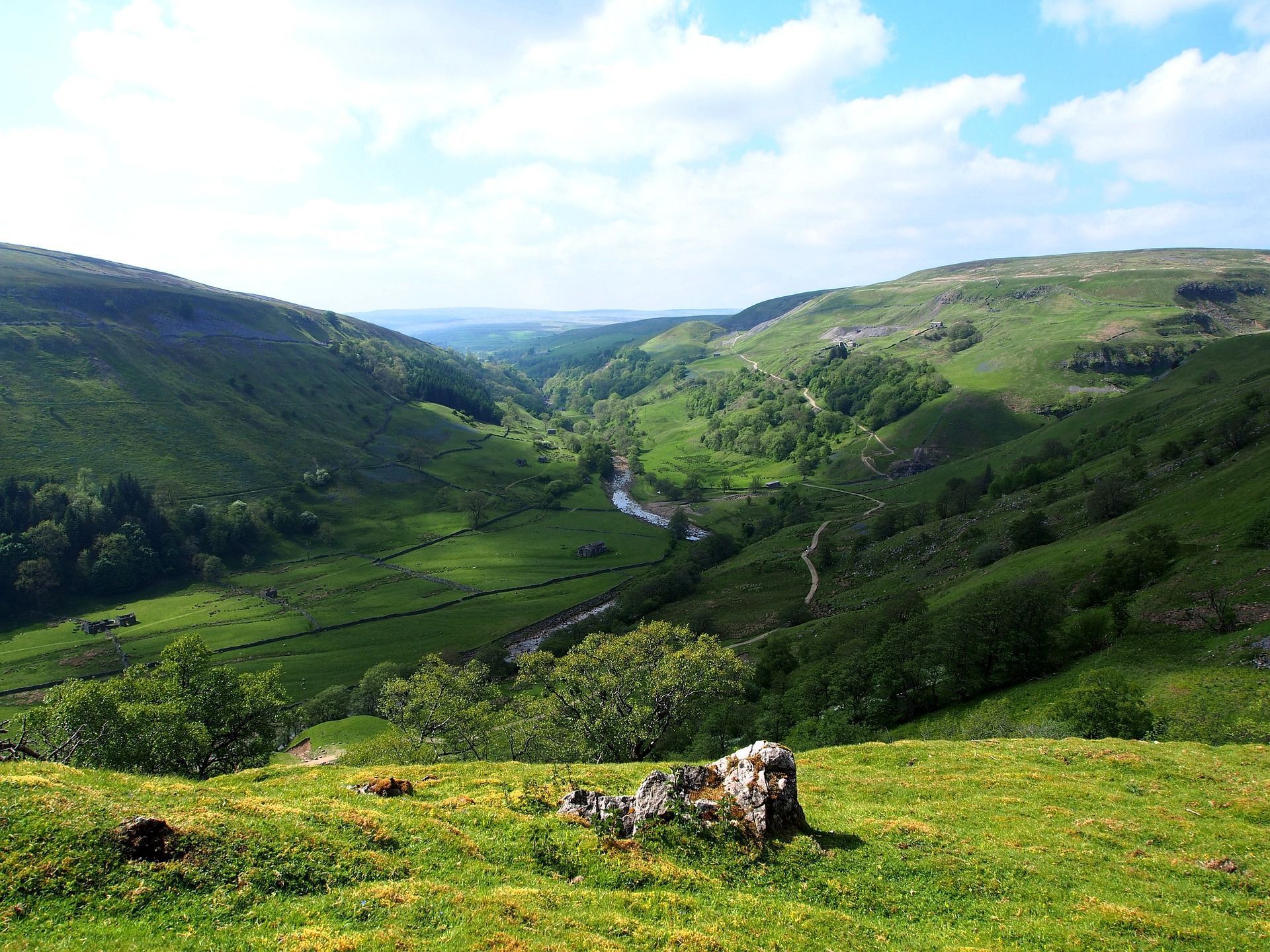 Green valley with a winding river, rolling hills, and a partly cloudy sky.