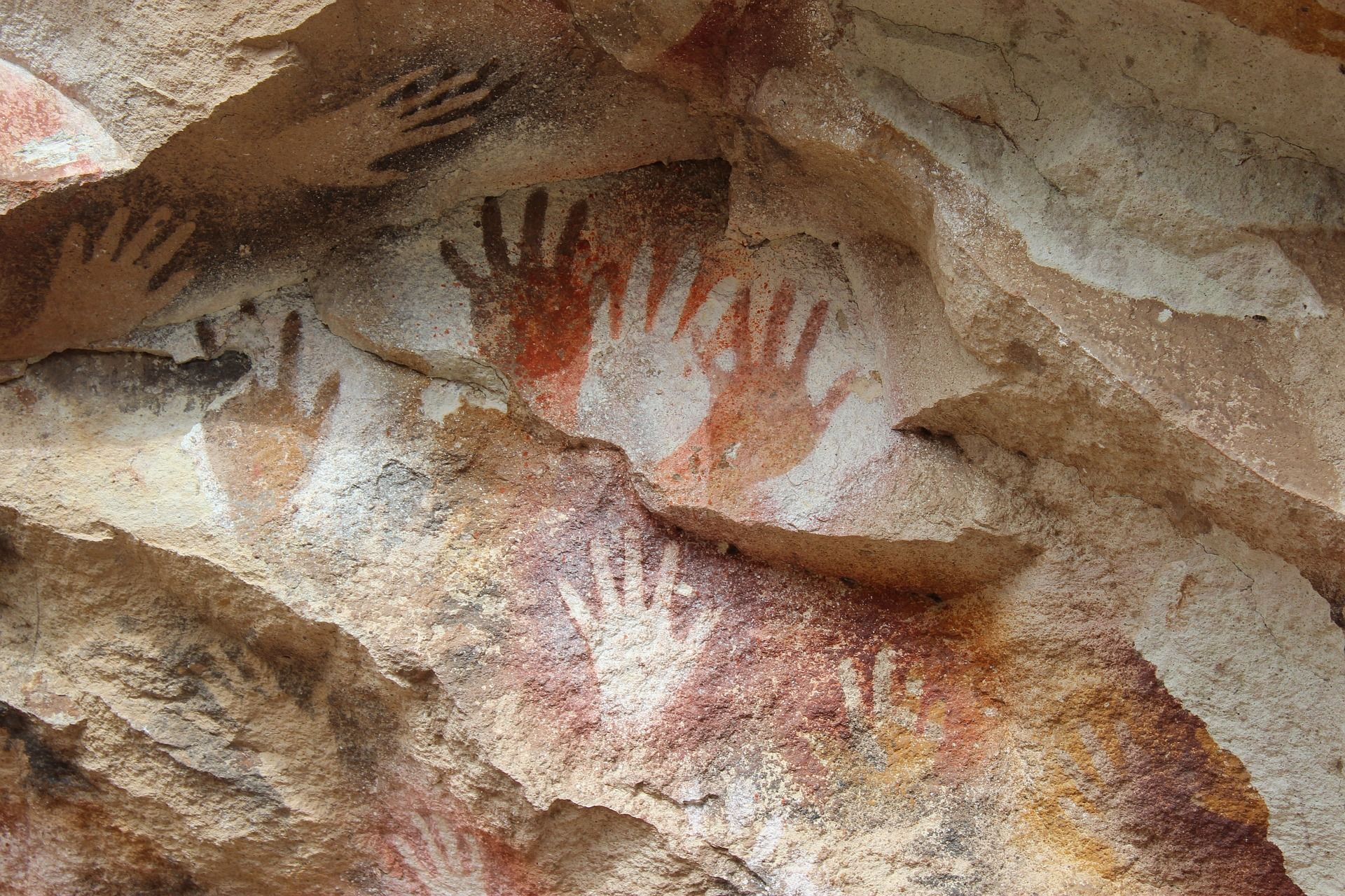 Hand stencils painted in red and black on a tan rock surface.