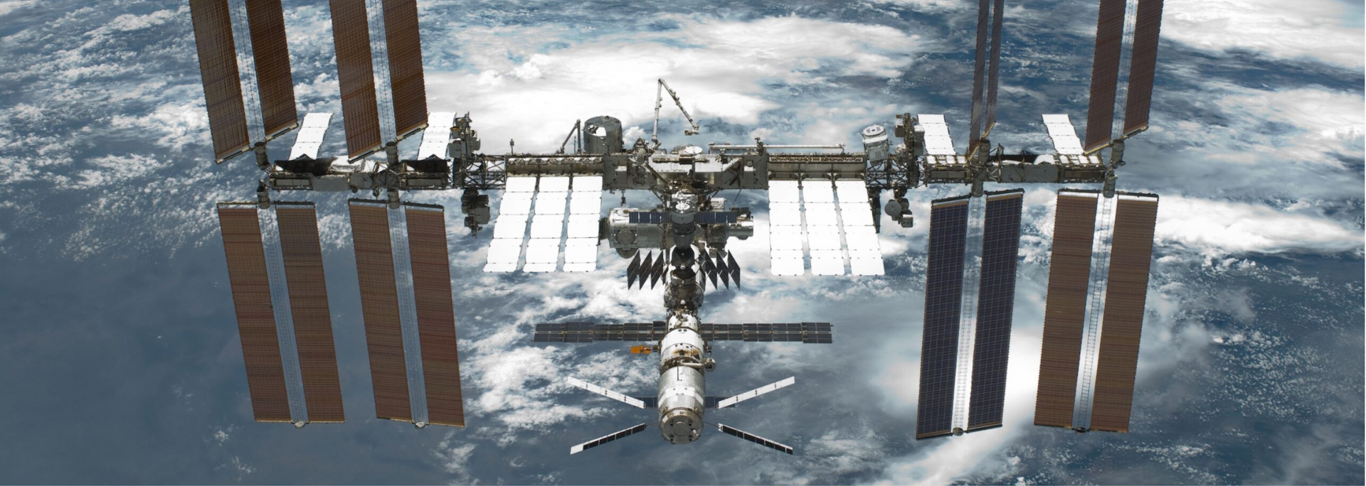 The International Space Station against the backdrop of Earth. Solar panels and docked spacecraft are visible.