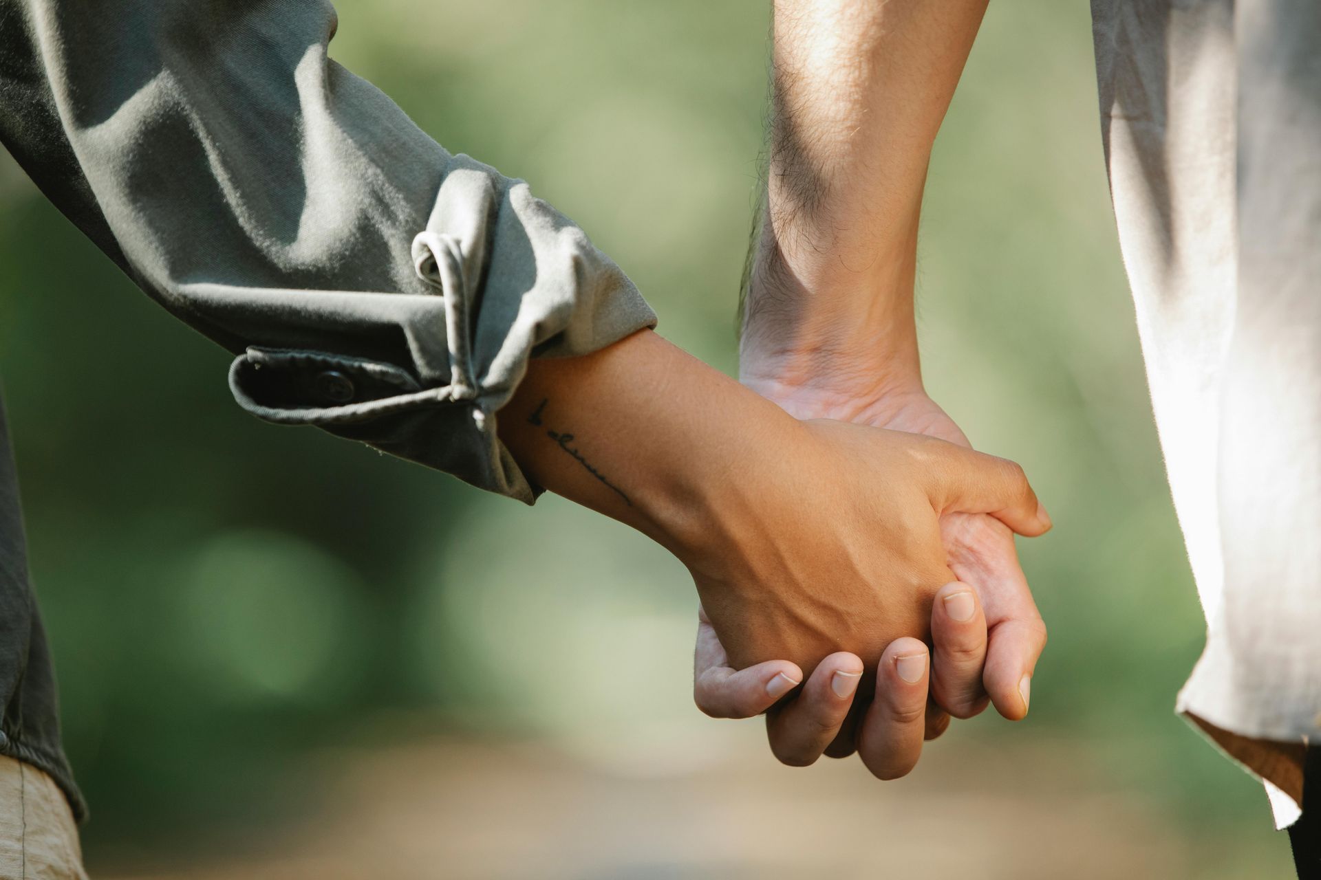 Two people holding hands, outdoors. One wears a green shirt, the other a white one.