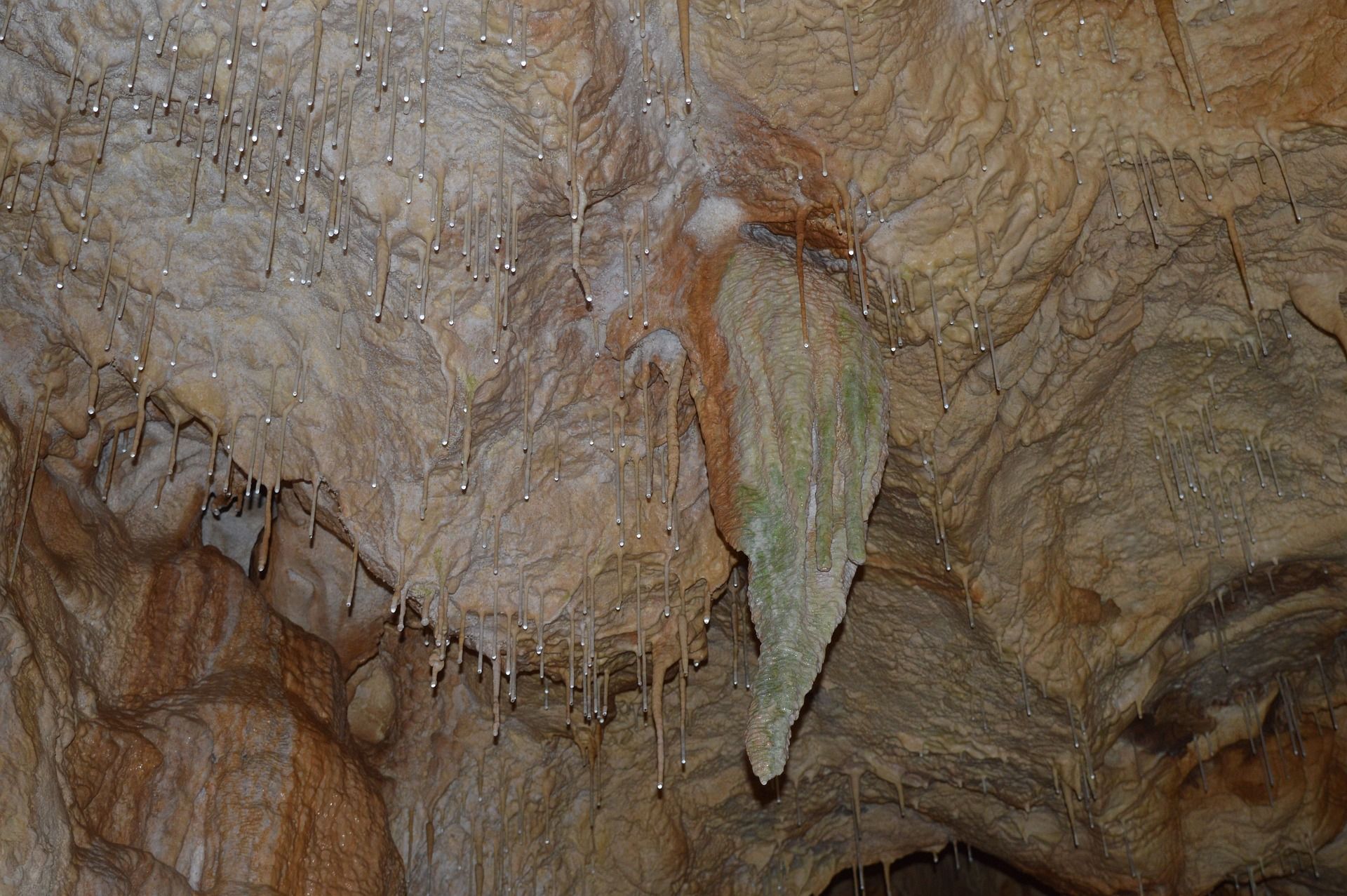 Cave interior with brown and tan rock formations, including stalactites and flowing, wavy patterns.