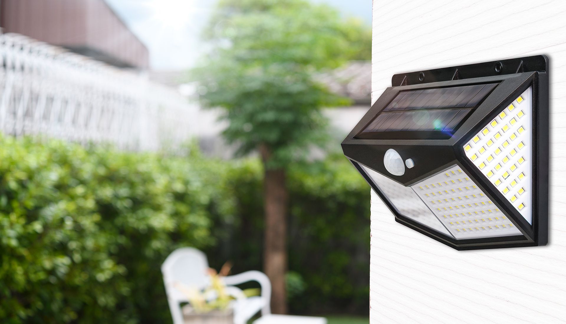 Solar-powered outdoor light with motion sensor mounted on a white wall in a yard.