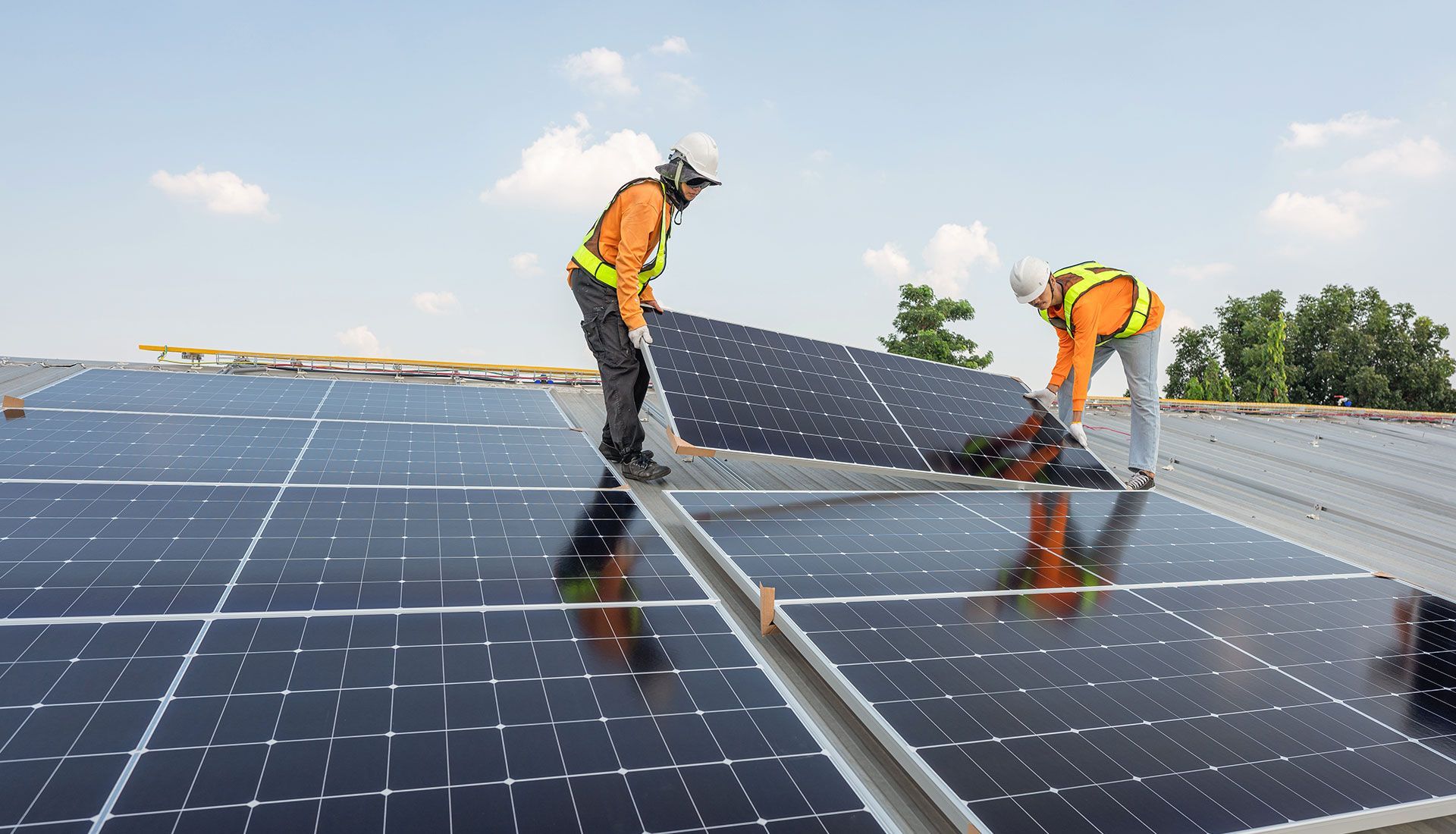 Two workers in safety vests installing solar panels on a rooftop on a sunny day.