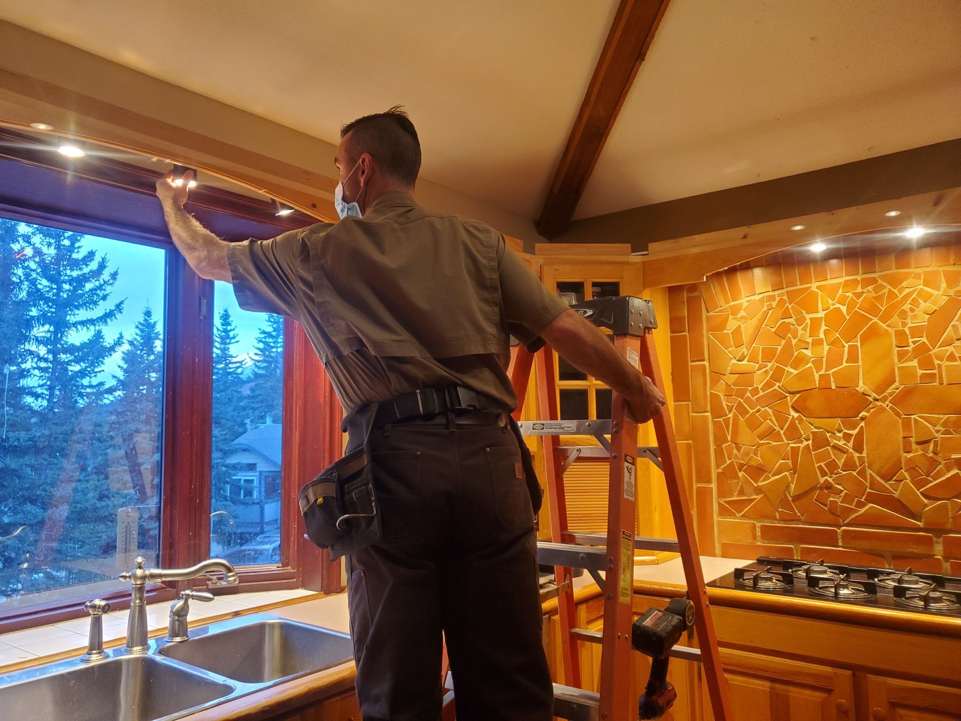 A man is standing on a ladder in a kitchen cleaning a window.