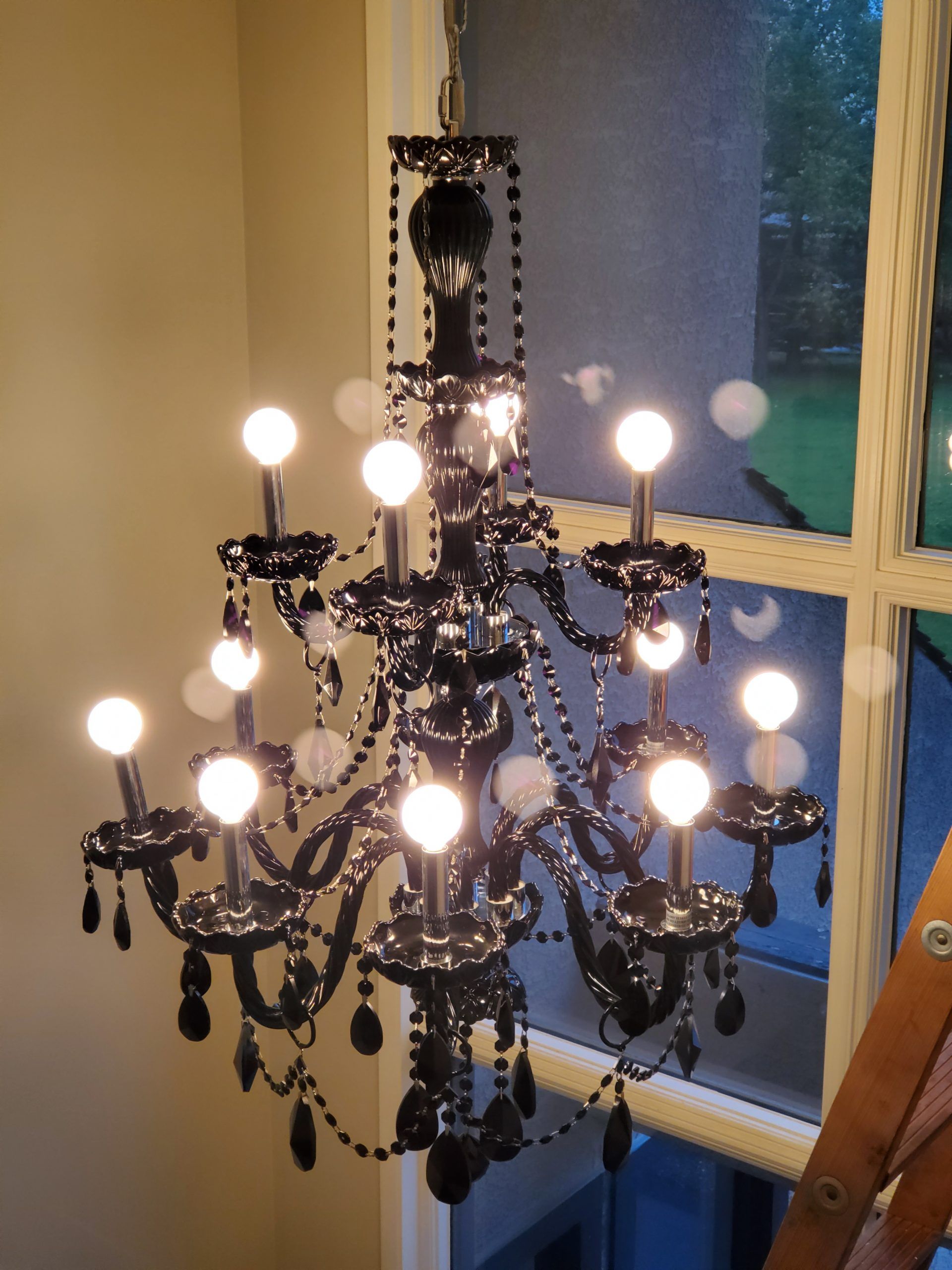 A black chandelier is lit up in front of a window