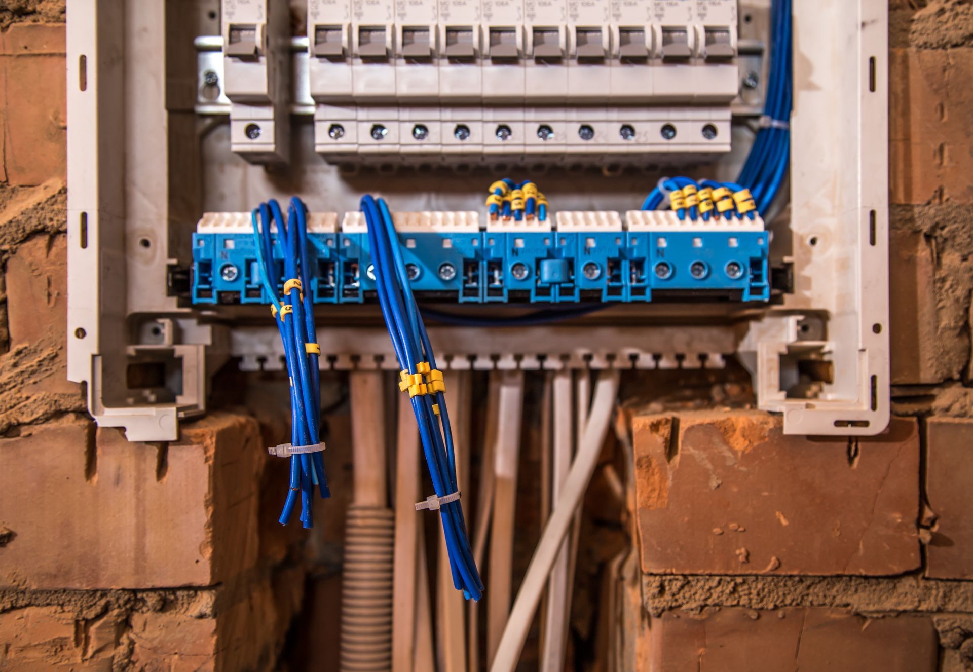 A close up of an electrical box on a brick wall with blue wires coming out of it.