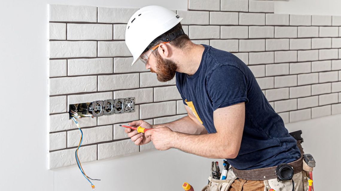 A man is working on an electrical outlet on a brick wall.